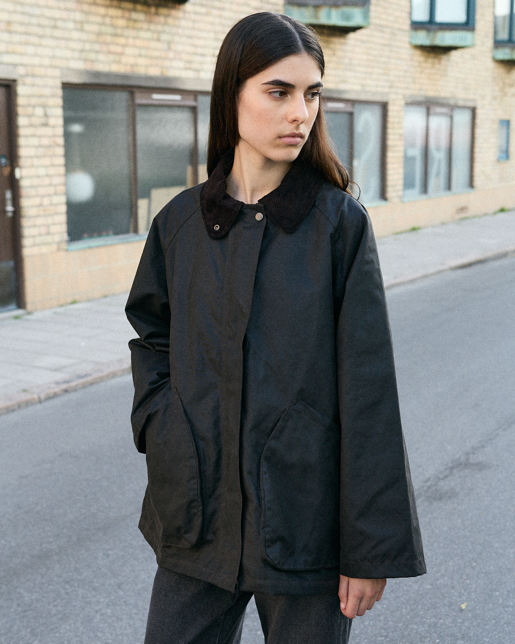 Model in a black waxed-cotton Brixtol jacket with a corduroy collar, on a city street
