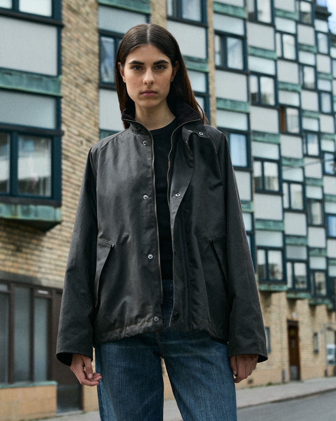Black Brixtol jacket worn open over a tee and jeans, apartment block behind