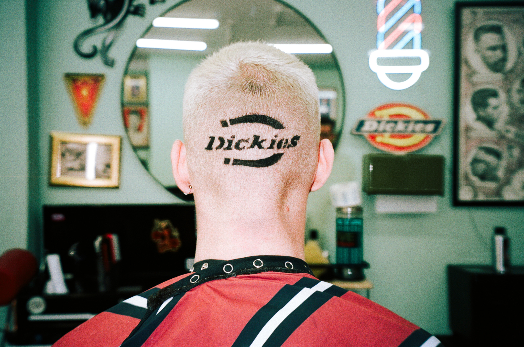 The Dickies logo shaved into the back of a bleached head, in a barbershop