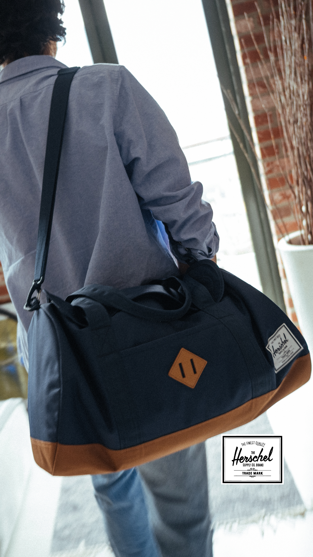 Navy Herschel duffle bag with a tan base, carried over the shoulder