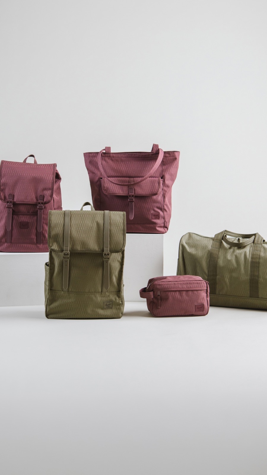 Herschel backpacks, tote and wash bag in burgundy and olive, on a white plinth