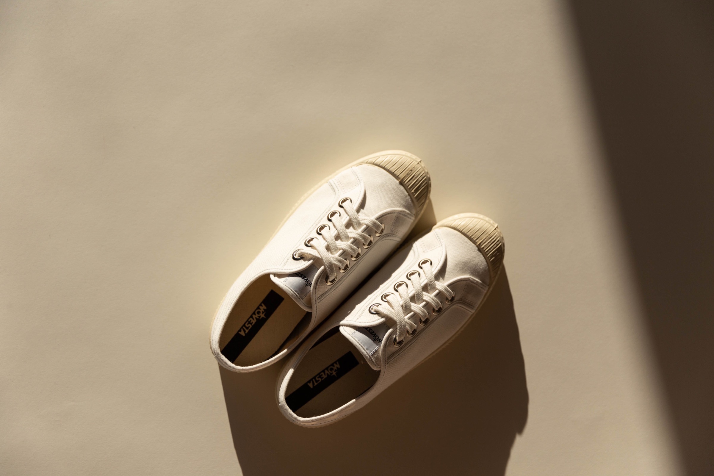 A pair of off-white Novesta sneakers in low sunlight, seen from above