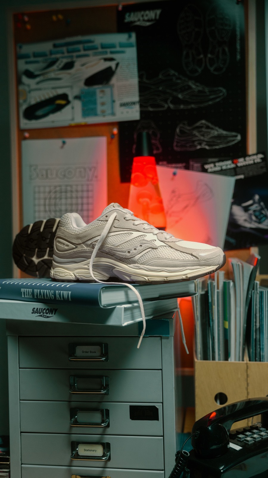 White Saucony sneaker on a filing cabinet in a design studio, a lava lamp glowing behind