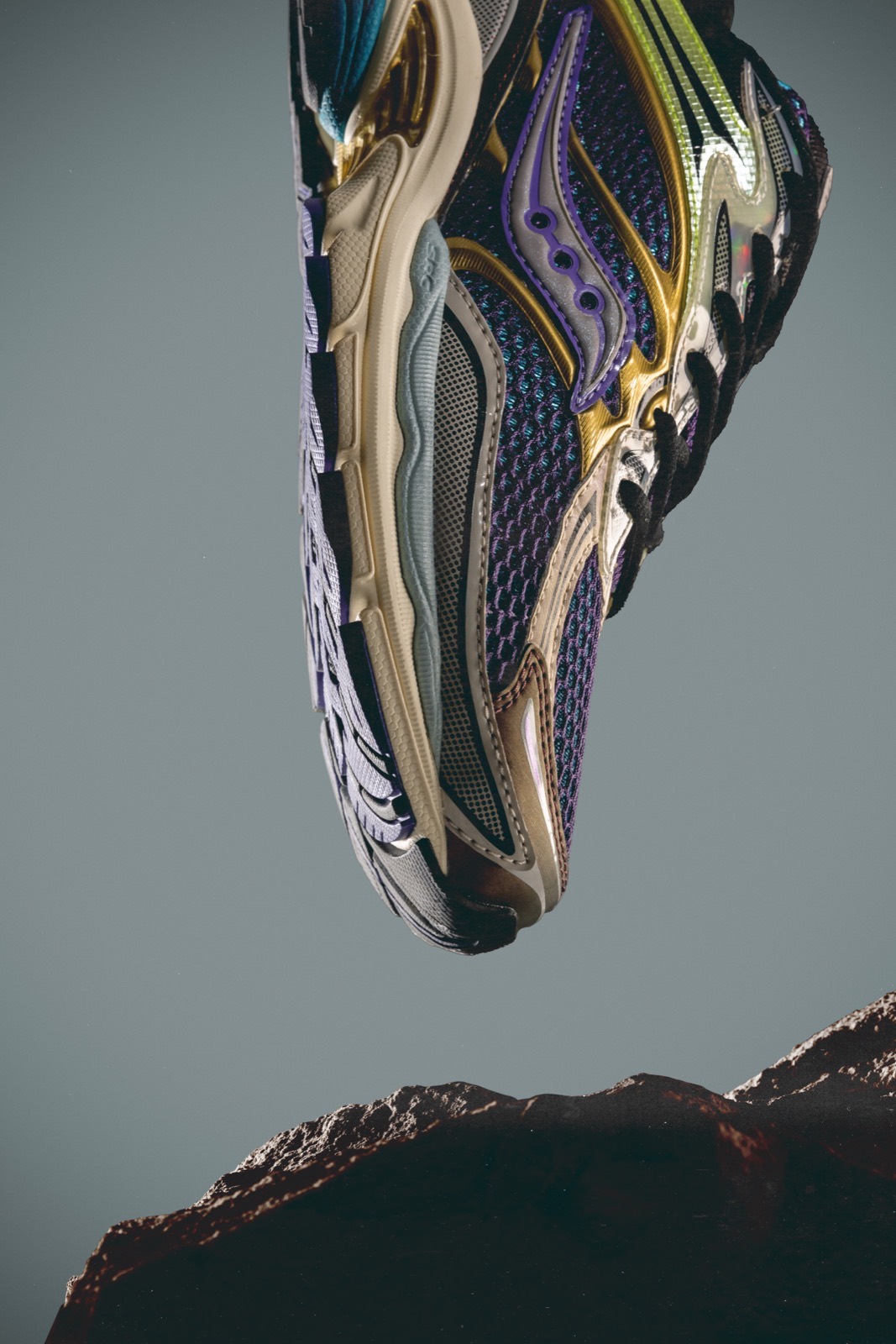 Multicoloured Saucony running shoe suspended above a rock