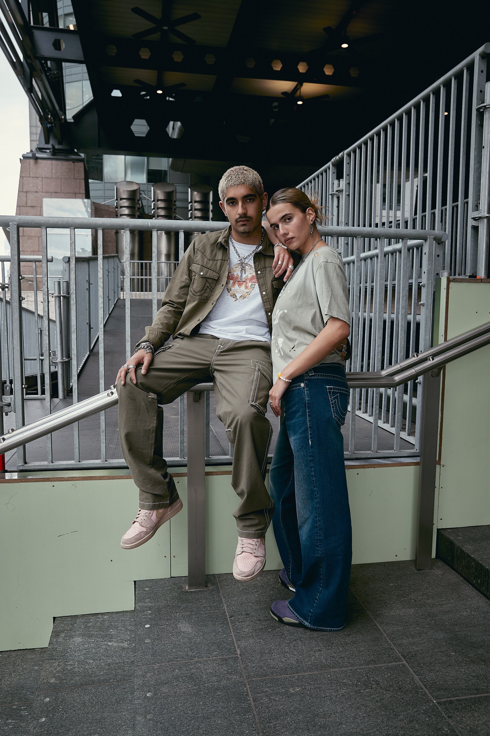 Two models in True Religion denim and utility wear on an outdoor staircase